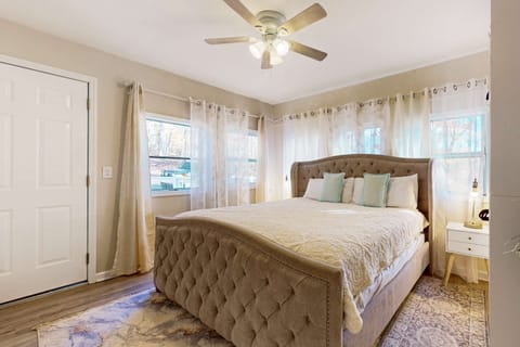 Bright primary bedroom featuring a plush king-size bed, large windows with natural light, and ceiling fan.