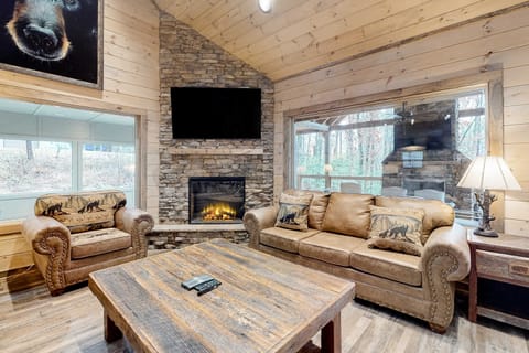 Rustic luxury living room featuring stone fireplace, smart TV, vaulted wood ceilings, and cozy seating. A perfect Smoky Mountain cabin retreat near Gatlinburg and Pigeon Forge.