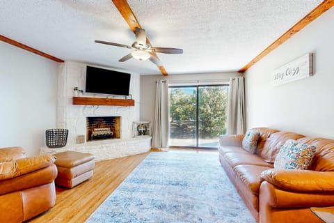 Bright living room with leather seating, smart TV, stone fireplace & sliding glass doors. Open-concept, family-friendly condo, with cozy cabin vibes, hardwood floors, natural light.