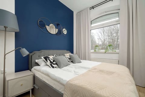 Bedroom with a double bed, blue accent wall, and large window providing natural light.