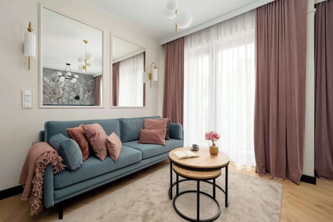 Cozy living area with a teal sofa, soft lighting and large windows with long curtains.