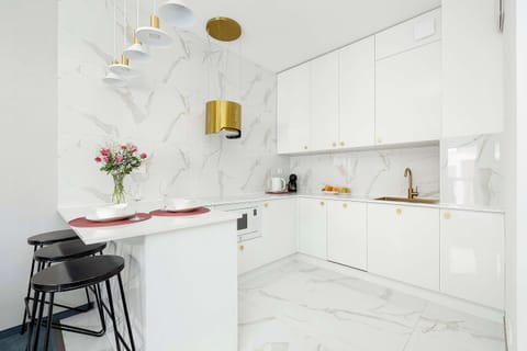 Another view of the white marble kitchen showcasing the countertop and elegant gold details. Decorative flowers add warmth to the modern design. The area looks pristine and stylish.