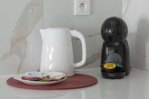 A small counter setup with a white electric kettle and a black coffee machine. A tray holds cups and a spoon, ready for use. The vignette feels tidy and practical.