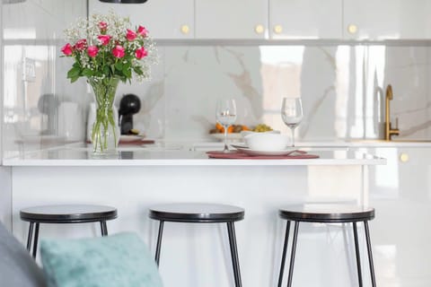 Another view of the white marble kitchen showcasing the countertop and elegant gold details. Decorative flowers add warmth to the modern design. The area looks pristine and stylish.