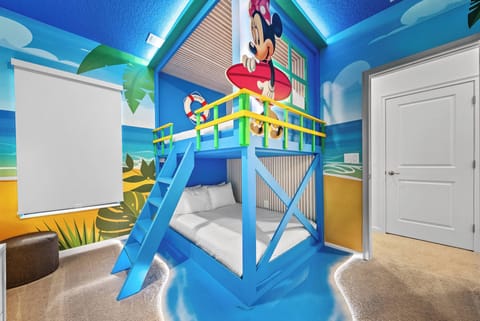 Welcome to a whimsical children's haven featuring a vibrant blue loft bed and lively beach murals. With a cozy lower sleeping area and soft carpeting, this playful retreat is perfect for little guests to enjoy adventures and.