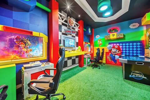 Step into a vibrant gaming haven, where bold red and blue walls set the stage for adventure. Enjoy the playful atmosphere with plush green carpet and dedicated gaming stations, perfect for hours of enjoyment and relaxation.