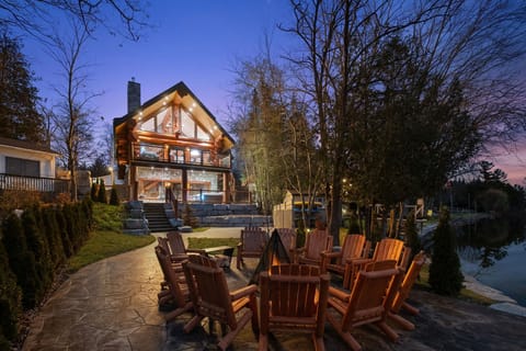 Luxury waterfront log home at dusk – spacious 3-level chalet with panoramic windows and outdoor living spaces.