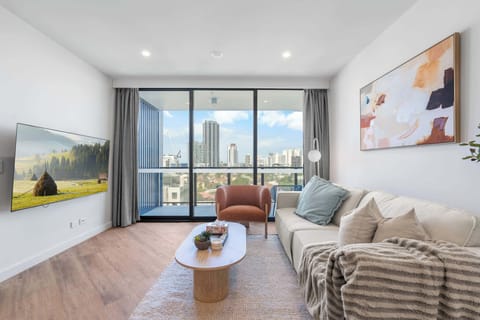 Serene Japandi-inspired living room featuring soft neutrals, textured layers and a full wall of glass framing Southport’s skyline and distant ocean views.