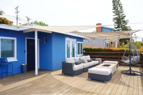 Spacious outdoor deck with comfortable lounge seating, a fire table, and a hanging chair, all set under shade sails and string lights perfect for relaxing or entertaining.
