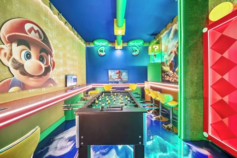 Enter a lively game room filled with bright colors and iconic characters that spark excitement. The bold blue ceiling and vibrant wall art create a fun ambiance, featuring a foosball table and stylish bar seating for socializing.