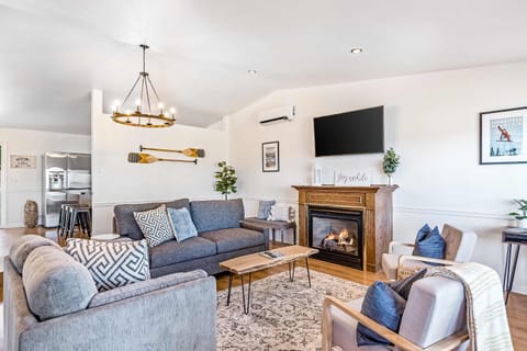 A bright, modern living room features cozy seating with a sofa bed, a fireplace beneath a wall-mounted TV, tasteful décor, and amenities including a foosball table for added entertainment.