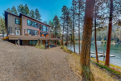 Sunny lakefront exterior with upper deck, orange umbrellas, floor-to-ceiling windows, and private boat dock steps away