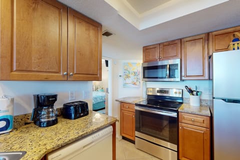 Cozy beach-stay kitchen featuring warm wood cabinets, granite counters, and stainless appliances. Fully stocked and perfectly placed for easy meal prep between relaxing oceanfront adventures.