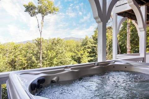 A luxurious hot tub sits beneath a charming covered deck overlooking lush forest scenery. The space features timber columns and open sky views, perfect for relaxing while immersed in nature.