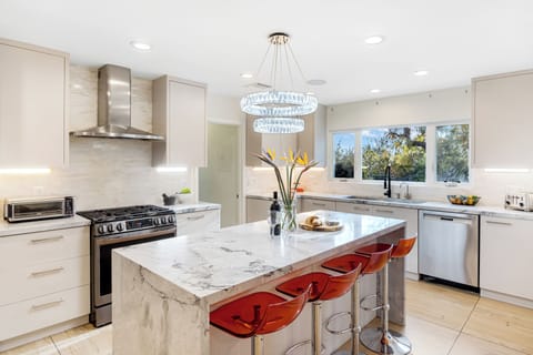 Bright, modern kitchen featuring a large central island with grey/white marble countertop and bright red bar stools.