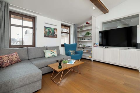 A bright open-concept living room with a sectional sofa and large TV. Warm wooden flooring adds comfort to the space.