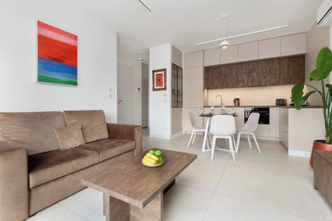 A modern living room with a wooden coffee table centered in front of a sofa. Large windows brighten the space while decorative pieces add personality. The simple layout keeps the room open and welcoming.