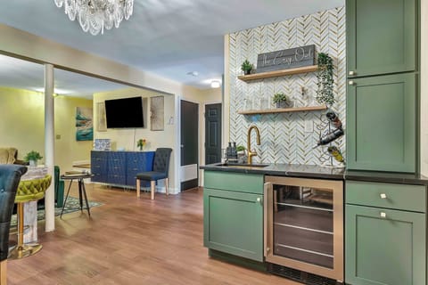 This beautifully designed wet bar features sage green cabinetry, a sleek wine fridge, gold fixtures, and open shelving with stylish accents—an inviting space to pour a drink, gather with friends, and enjoy the good times.