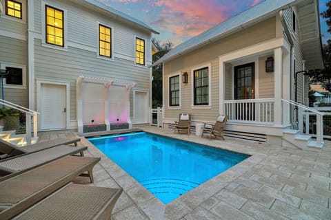 A private courtyard pool glows in the twilight, framed by elegant white columns and surrounded by inviting lounge chairs—perfect for evening swims under pastel skies.