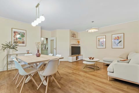 Bright and inviting living area featuring a spacious L-shaped sofa and a modern dining space. Large windows fill the room with natural light, creating the perfect setting to relax after exploring Luxembourg.