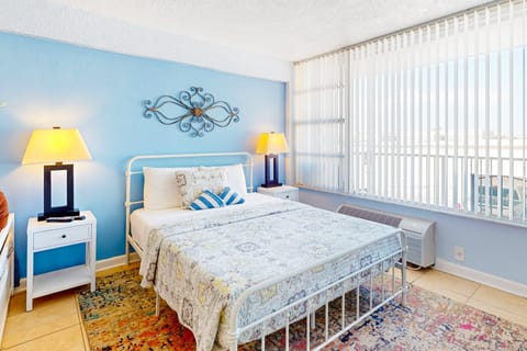 Inviting beach-style bedroom with soft blue accents, cozy bedding, and sunlit windows. A perfect coastal stay for relaxing after a day by the ocean.