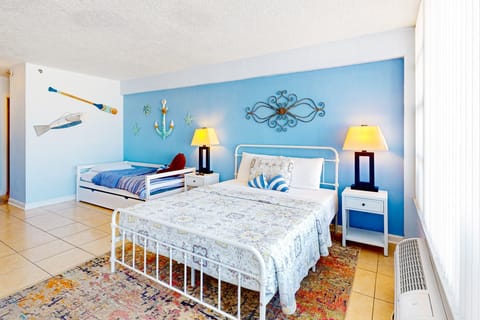 Charming beach stay bedroom featuring a comfy queen bed and trundle, coastal décor, warm lighting, and airy blue tones—perfect for a relaxing oceanside getaway.