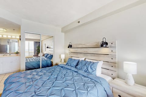 Bright beach-inspired bedroom featuring a plush king bed, modern lighting, and mirrored closet. Enjoy a relaxing stay with soothing coastal décor, steps from ocean views and sandy shores.