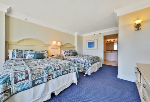 Inviting beach-stay room featuring two comfy beds with coastal bedding, warm lighting, and easy access to a bright vanity and bath area—perfect for a relaxing coastal getaway.