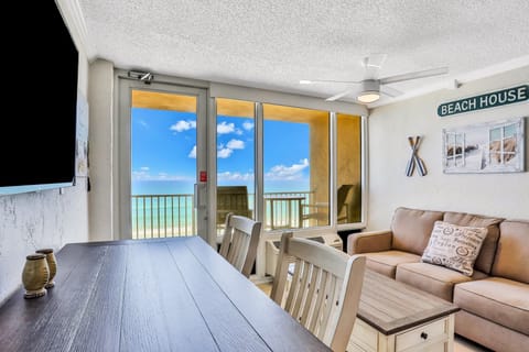 Bright oceanfront living space featuring dining area, cozy seating, and floor-to-ceiling windows opening to a private balcony. Enjoy a relaxing beach stay with stunning ocean views, coastal décor, and easy access to sun and sand.