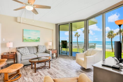 Relax in this sunny oceanfront living room featuring cozy seating, modern décor, and stunning beach views through floor-to-ceiling windows—perfect for a refreshing coastal stay.
