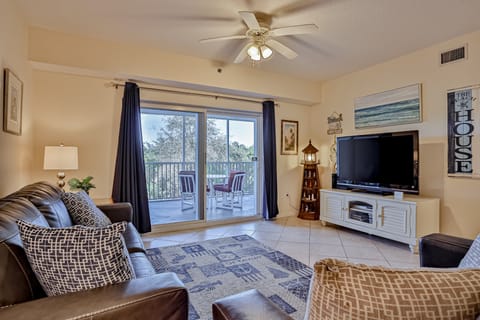 Bright coastal living room with comfy seating, flat-screen TV, and sliding doors to a private balcony. Perfect for a relaxing beach stay, this inviting space blends comfort and seaside charm just steps from your coastal getaway.