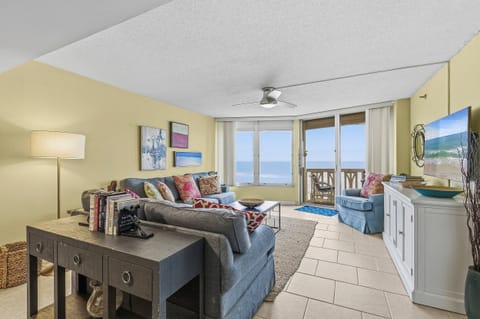 Bright oceanfront living room featuring cozy seating, coastal décor, and direct access to a private balcony. Enjoy panoramic beach views, natural light, and a relaxing beach stay just steps from the shore.