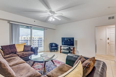 Relax in this sunlit living area featuring comfortable seating, a flat-screen TV, and balcony access. Perfect for a beach stay, this coastal condo offers space to unwind after sandy days and ocean adventures.