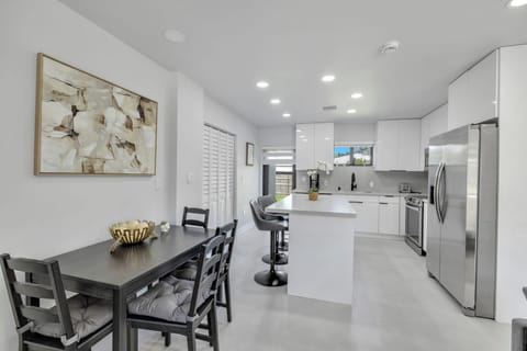 Bright and airy, this modern kitchen and dining area features sleek cabinetry, stainless steel appliances, a large island with seating for three, and a dining table for four. Enjoy natural light, easy indoor-outdoor flow, and a perfect space for cook