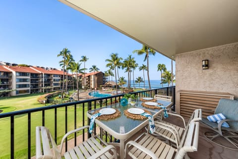 Private balcony with outdoor dining set, offering panoramic views of lush lawns, palm trees, and the nearby ocean under a bright blue sky.