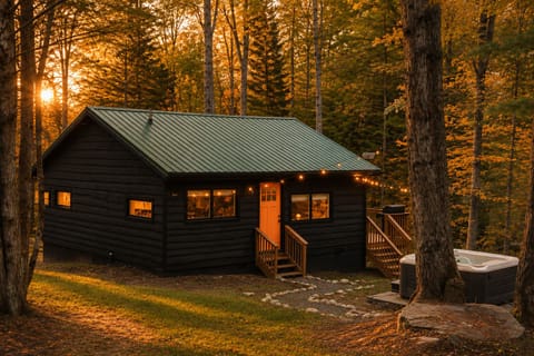 The private hot tub sits nestled beside a large tree, offering a perfect spot for starlit soaks. A stone path leads to the bright orange front door, where string lights illuminate your way to this quiet retreat.