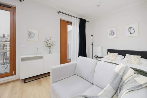 A bright living room with a white sofa placed against a clean, minimalist wall. Light wooden flooring adds warmth to the airy space. Subtle wall décor keeps the room elegant and uncluttered.