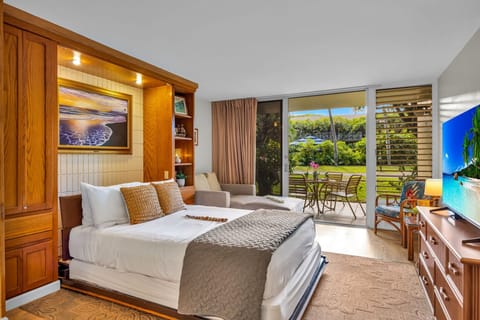 Relax in a bright bedroom featuring a comfortable bed, warm wood accents, and sliding glass doors that open to a private lanai with garden views.
