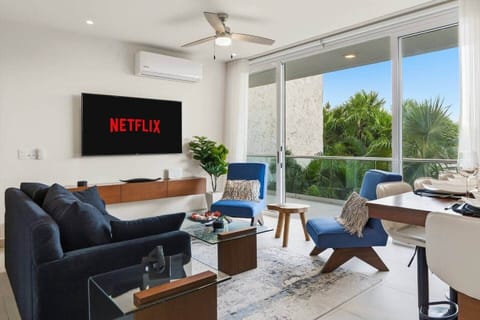A welcoming living room featuring a comfortable sofa bed, large smart TV, and wide sliding glass doors that open to a private balcony with lush jungle and pool views. A perfect spot to relax, stream your favorites, and enjoy the scenery.