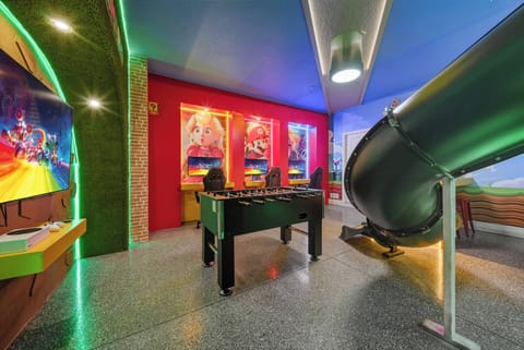 Enter a lively playroom adorned with colorful art and a fun slide, inviting laughter and joy. The shiny flooring and sleek foosball table create an energetic space ideal for family bonding and entertainment.