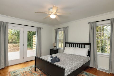 This bright bedroom features a dark wood bed frame with patterned linens and a colorful area rug. Large glass doors open directly to the back deck, allowing for plenty of natural light and easy outdoor access.
