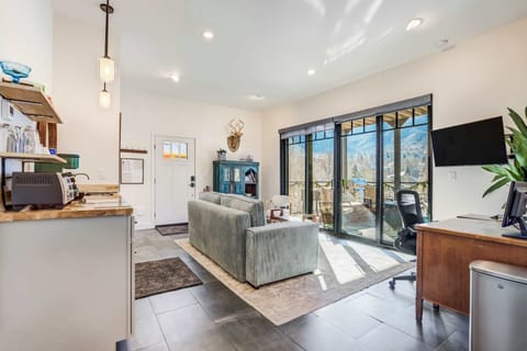 The open-concept living area blends modern seating, warm wood textures, and a full wall of sliding glass doors that draw your attention straight to the sweeping mountain landscape outside.