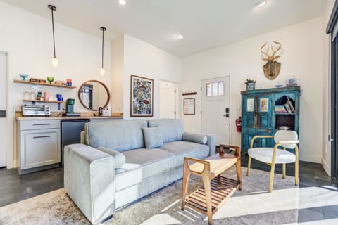 A cozy arrangement of the sofa, accent chair, wooden coffee table, blue cabinet, and visible kitchenette creates a warm gathering space framed by sliding glass doors facing the mountains.