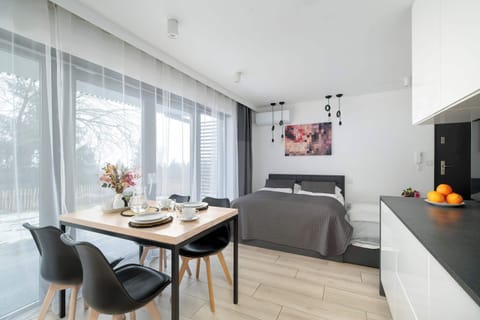 A bright dining and living area with large windows letting in natural light. A small table is set for a meal beside a cozy sitting space.