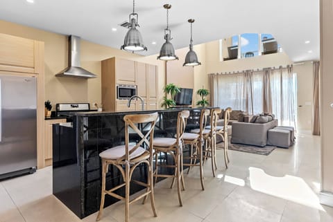 This stylish kitchen boasts sleek black countertops and light wood cabinetry for a warm contemporary feel. Pendant lights brighten the spacious island, and large windows invite natural light, creating an inviting atmosphere for.