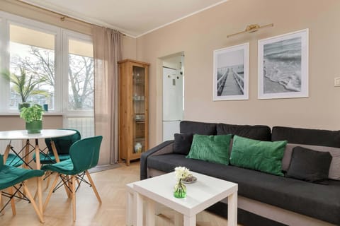 A bright living room with a green sofa set, a small dining table, and framed artwork on the wall.