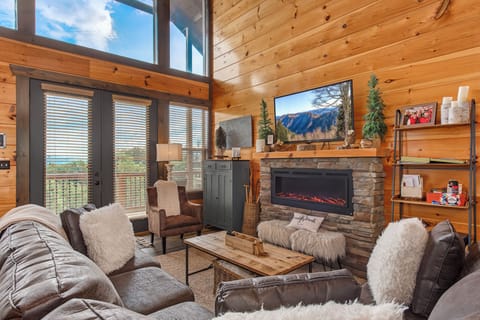 Imagine yourself sinking into plush seating by a crackling fireplace, mountain views framing your relaxation in this bright, airy cabin-style living room with soaring windows and natural warmth.