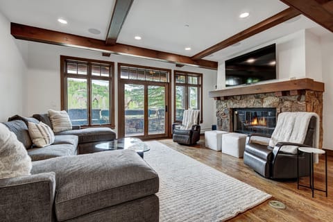 Relax in the inviting living room, adorned with a warm stone fireplace and panoramic windows that bring the beauty of the alpine landscape indoors.