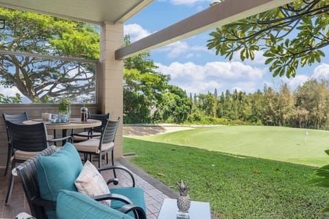 Relax on a shaded lanai with plush seating and a dining table, overlooking a lush green lawn and tropical trees.