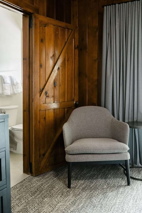 Barn-style bathroom door beside a soft chair and gray curtains